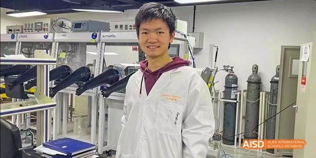 A student from Beijing No.2 Middle School wearing a white lab coat and smiling at the camera, standing in a laboratory setting.