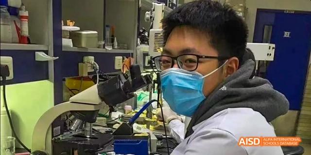 A student from Beijing No.2 Middle School wearing a face mask, working at a station with technical equipment and a microscope in a science lab.