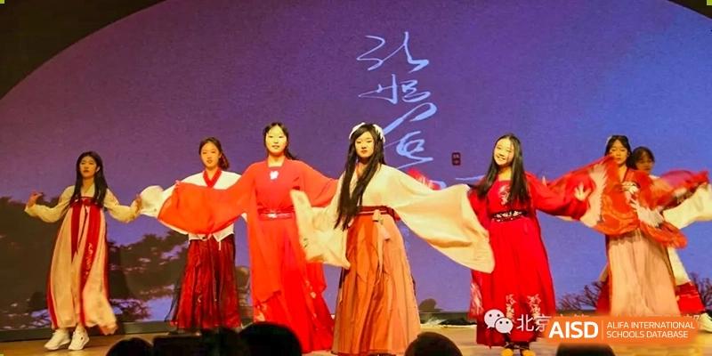 Two students from Beijing No.2 Middle School performing a traditional Chinese dance in red and white costumes on a stage with large calligraphy writing.