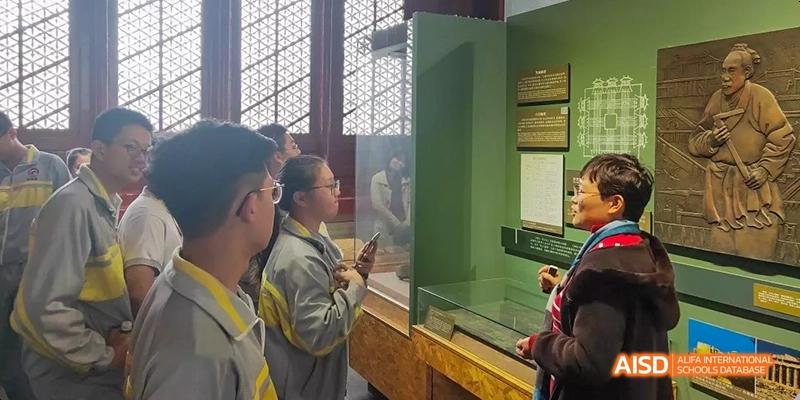 Students from Beijing No.2 Middle School looking at an artifact or display case behind a glass partition inside a well-lit exhibition hall.