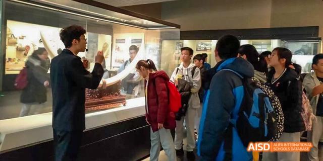 Several students from Beijing No.2 Middle School in a museum, looking closely at an artifact displayed inside a glass case.