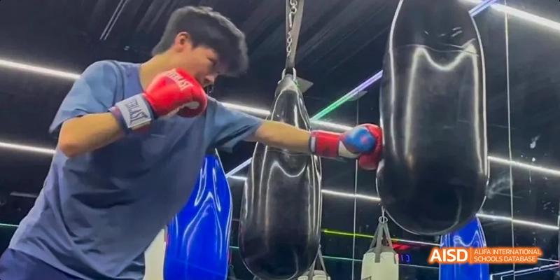 A student from Beijing No.2 Middle School practicing boxing, punching a heavy bag while wearing red boxing gloves.