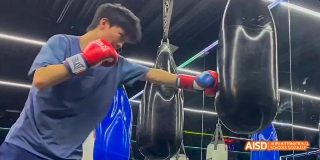 A student from Beijing No.2 Middle School practicing boxing, punching a heavy bag while wearing red boxing gloves.