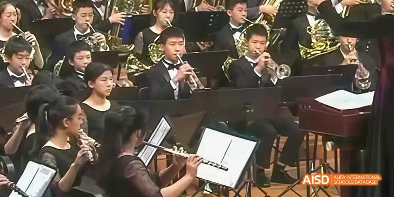 A close-up of a student from Beijing No.2 Middle School playing a flute or similar woodwind instrument in an orchestra or band setting.