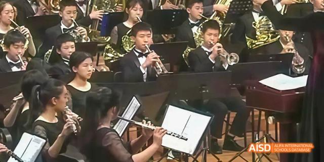 A close-up of a student from Beijing No.2 Middle School playing a flute or similar woodwind instrument in an orchestra or band setting.
