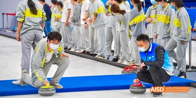 A close-up of students from Beijing No.2 Middle School in their sportswear, lined up on a dark mat next to a blue surface with a curling stone visible in the foreground.