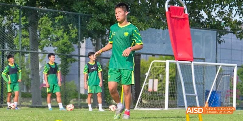 Students from Beijing No.2 Middle School playing soccer/football on a green turf field, with one student in a bright green uniform visible.