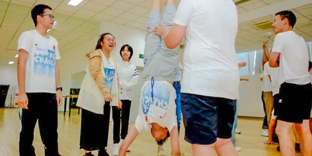 Students from Beijing No.2 Middle School participating in an indoor physical activity, with one student doing a handstand while others watch and smile.