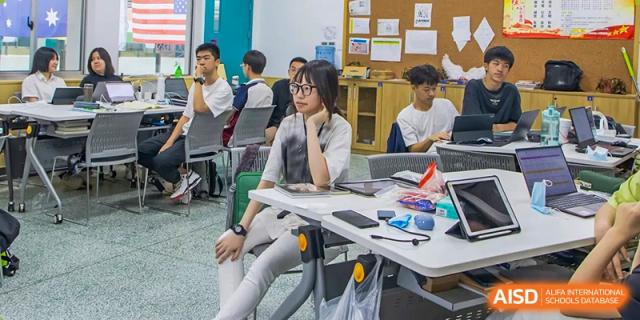 A female student from The International School of Rhodes working on a laptop at a table in a classroom.