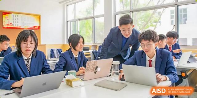 A teacher from The International School of Rhodes assisting a student with work on a laptop at a table.