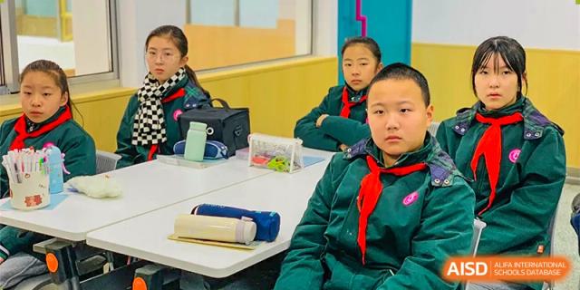 A young student from The International School of Rhodes in uniform with a red scarf posing in a classroom.