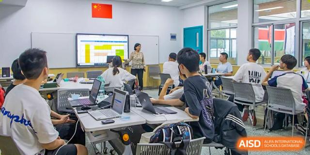 Students from The International School of Rhodes working together on laptops and desktops in a modern classroom or lab.