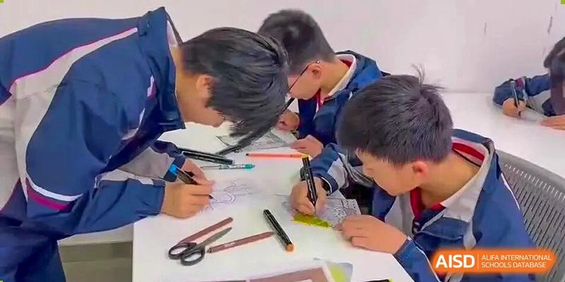 Students from The International School of Rhodes collaborating on a drawing or writing project at a desk.