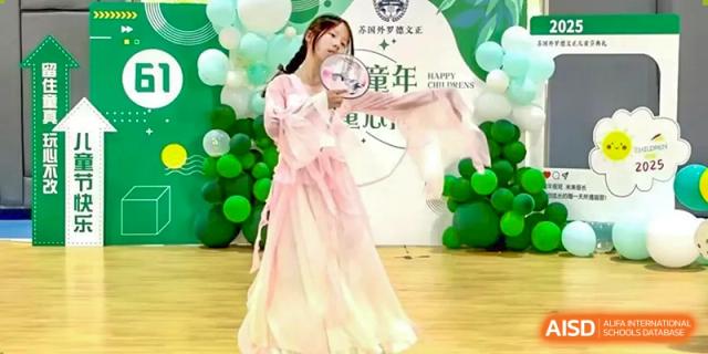 A female student from The International School of Rhodes in a traditional dress posing with a prop against a celebratory background.