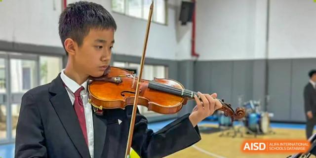 A student from The International School of Rhodes in a suit playing the violin indoors.