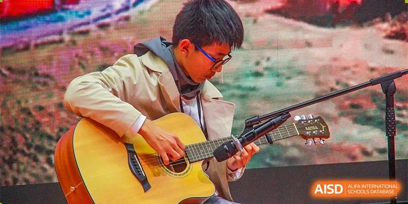 A student from The International School of Rhodes playing an acoustic guitar outdoors.