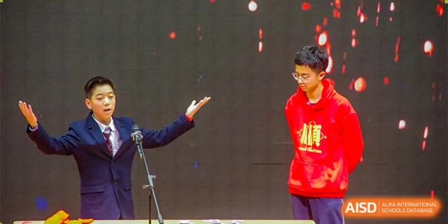 A student from The International School of Rhodes giving a speech or presentation on a stage with a large screen in the background.