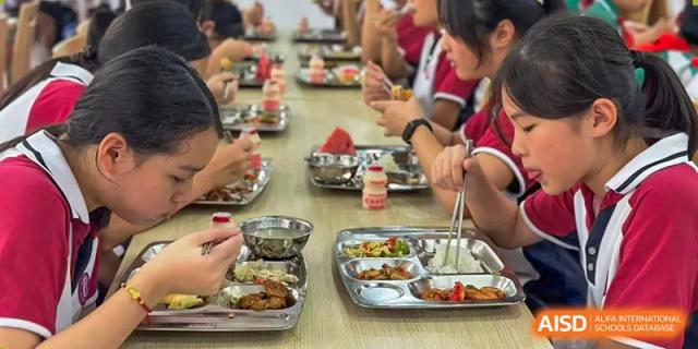Students from The International School of Rhodes eating their meals from metal cafeteria trays at a table.