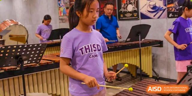 A young female student from Tsinghua International School Daoxiang Lake playing a percussion instrument, possibly a xylophone or marimba.
