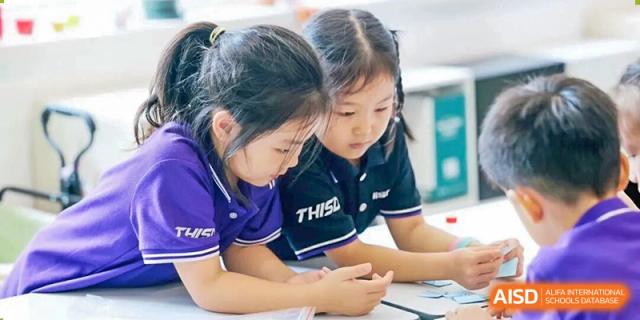 Two female students from Tsinghua International School Daoxiang Lake in uniform working together on an assignment at a desk.