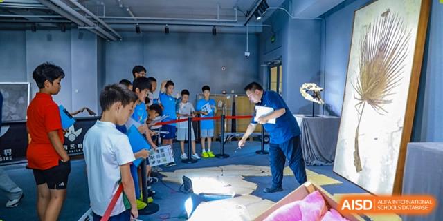 Students from Tsinghua International School Daoxiang Lake working on a hands-on project, possibly robotics or engineering, with a teacher supervising.