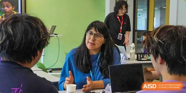 A female staff member or teacher from Tsinghua International School Daoxiang Lake leaning forward and speaking with a colleague or student.