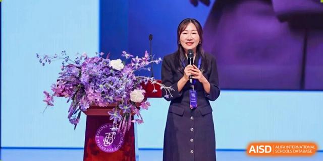 A female speaker holding a microphone and standing next to bouquets of flowers on a stage at an event for Tsinghua International School Daoxiang Lake.
