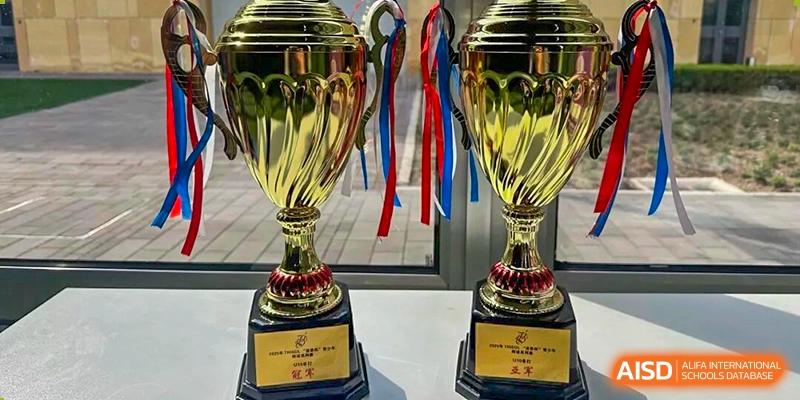 A close-up of two large gold trophies with red and blue ribbons, likely awards won by Tsinghua International School Daoxiang Lake.