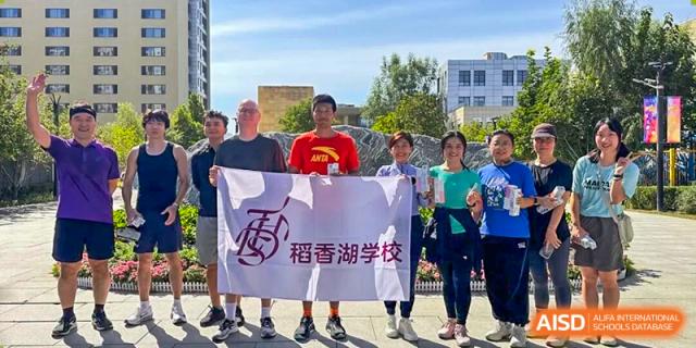 A group of adults holding a Fuxing Lake School banner outdoors, possibly a partner school event at Tsinghua International School Daoxiang Lake.
