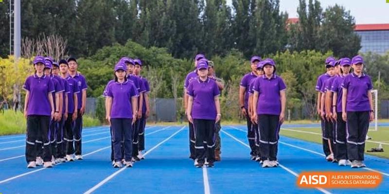 Students from Tsinghua International School Daoxiang Lake marching in purple and white uniforms on a blue sports track.