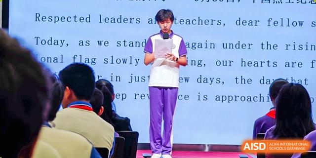 A student from Tsinghua International School Daoxiang Lake wearing a purple uniform and reading from a script on a stage.