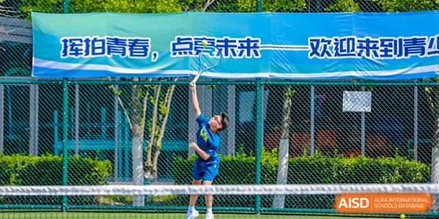 A student from Tsinghua International School Daoxiang Lake serving or hitting a tennis ball on an outdoor court.