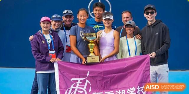 A group of happy students from Tsinghua International School Daoxiang Lake posing with a trophy and a purple banner after a competition victory.
