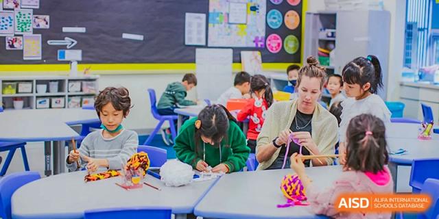 Primary school students at American International School of Guangzhou (AISG) focus on a writing or drawing activity while seated at small desks in a classroom.