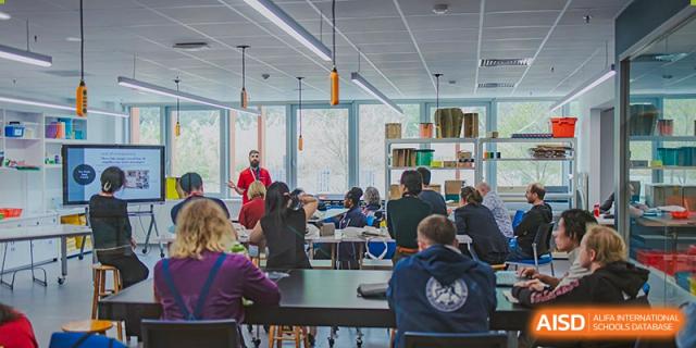 High school students at American International School of Guangzhou (AISG) collaborate and work on laptops and books around a large table in an open learning area.
