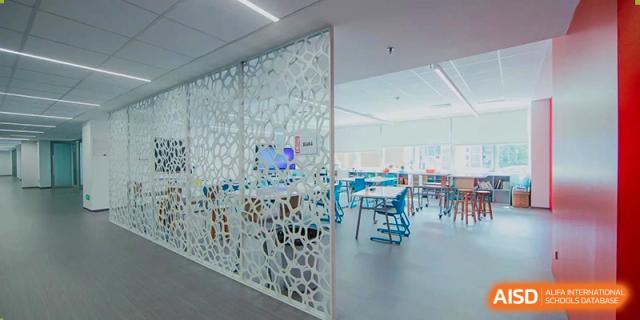 A modern, brightly-lit learning commons or library space at American International School of Guangzhou (AISG), featuring a decorative white screen partition.