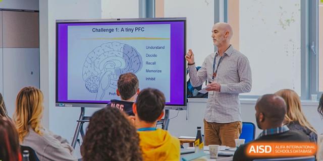 A teacher at American International School of Guangzhou (AISG) gives a presentation on a screen showing a diagram of the human brain to a group of students.