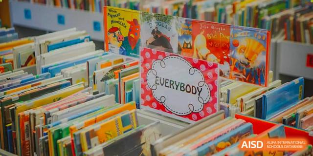 A close-up of a shelf in the library at American International School of Guangzhou (AISG) showing various children's books, with one book labeled "EVERYBODY."