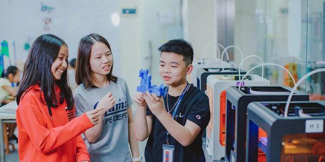 Two students at American International School of Guangzhou (AISG) examine a plastic object, likely a model or 3D print, in a classroom or lab setting.