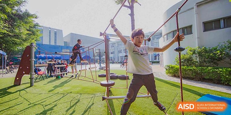 A male student navigating an outdoor ropes course or agility structure at the American International School of Guangzhou (AISG).