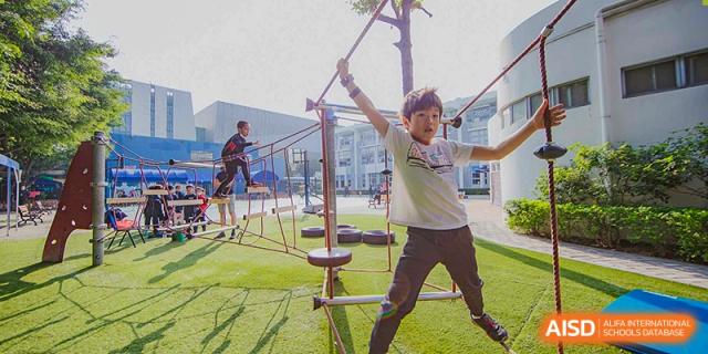 A male student navigating an outdoor ropes course or agility structure at the American International School of Guangzhou (AISG).