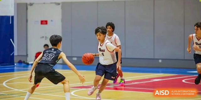 Male students playing basketball on an outdoor court during a game or practice session at the American International School of Guangzhou (AISG).
