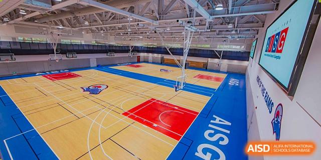 A spacious, well-lit indoor gymnasium or multipurpose court with the initials AISG visible on the floor at the American International School of Guangzhou (AISG).