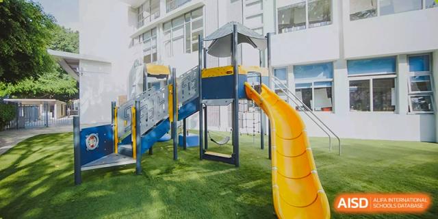 A modern outdoor playground featuring yellow slides and climbing structures on green turf at the American International School of Guangzhou (AISG).