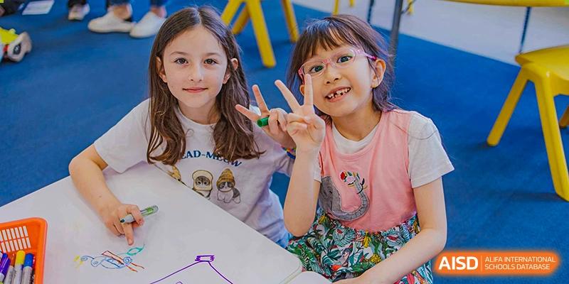 Two smiling young female students posing happily for the camera, showing a peace sign, at the American International School of Guangzhou (AISG).
