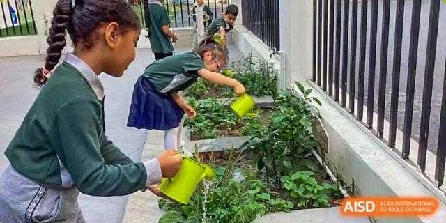 A student in a school uniform watering plants in an outdoor garden with a green watering can at Britannia International School Guangzhou.