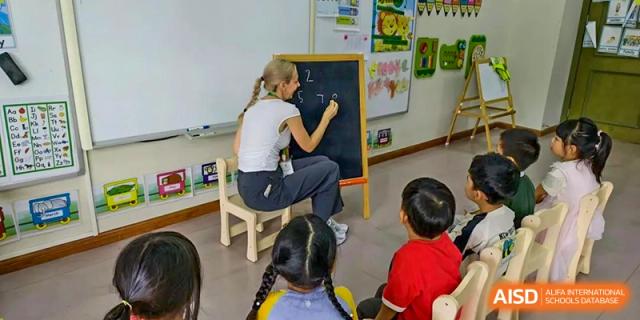 A female teacher crouching down to write or draw on a small blackboard while students watch at Britannia International School Guangzhou.