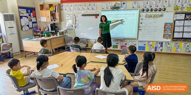 A female teacher pointing to a presentation on an interactive whiteboard while instructing students seated at desks at Britannia International School Guangzhou.