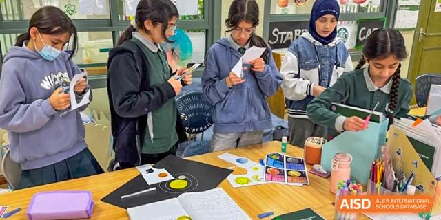 A group of students gathered around a table examining materials and papers during a project or team activity at Britannia International School Guangzhou.