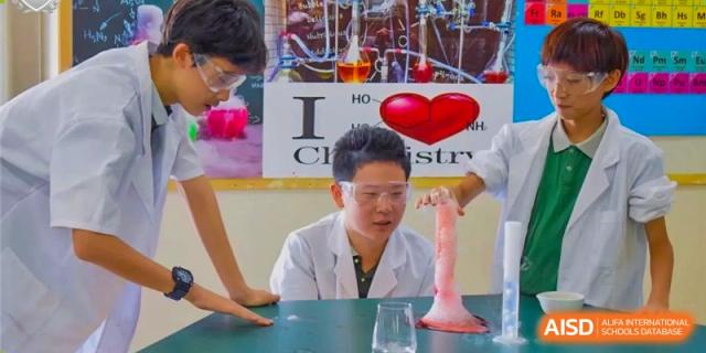 A student wearing safety glasses and a lab coat conducting a science experiment with a beaker and a pink funnel at Britannia International School Guangzhou.